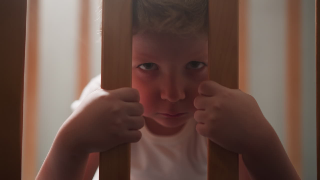 심각한 작은 소년은 산책로의 나무 바를 잡고 간식을 먹습니다.