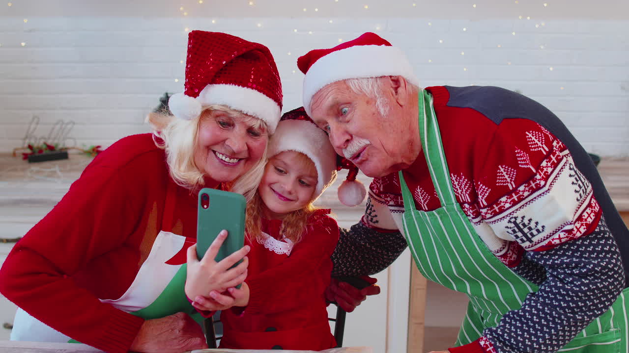 abuelos mayores con un niño nieta tomando una foto de selfie en el teléfono móvil en la cocina de navidad