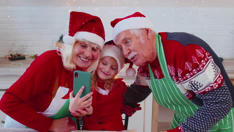 Senior-grandparents-with-granddaughter-kid-taking-selfie-photo-on-mobile-phone-at-Christmas-kitchen