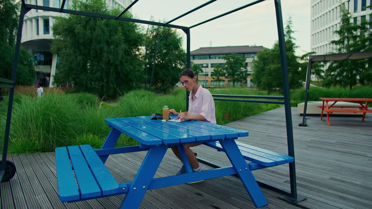 Una donna scrive a un tavolo da picnic blu in un parco all'aperto