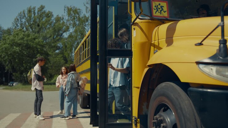 Two school children going out schoolbus. Teenagers standing at bus talking.
