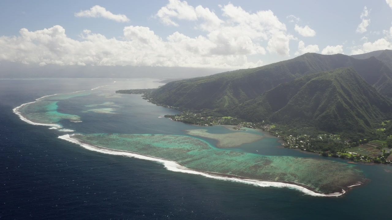 Wide aerial drone shot over the Teahupoo coral reef pass, Tahiti, layered shades of turquoise lagoon fading into deep blue open ocean.