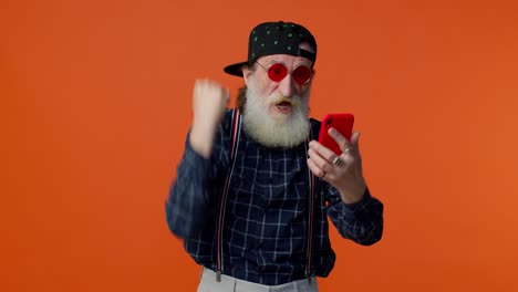 Elderly-bearded-man-use-mobile-phone-browsing-online-say-wow-yes,-big-win-news-doing-winner-gesture