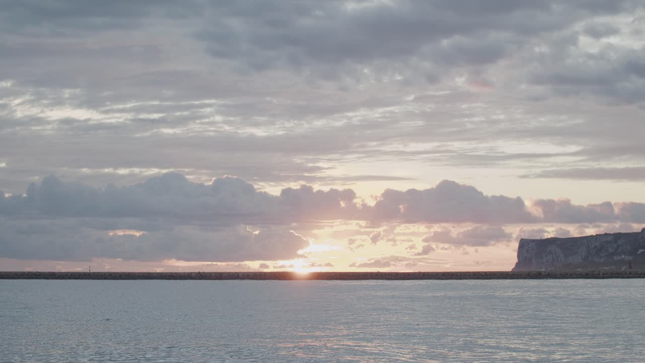 timelapse de 4k del sol saliendo detrás de las nubes en el mar con la montaña al fondo
