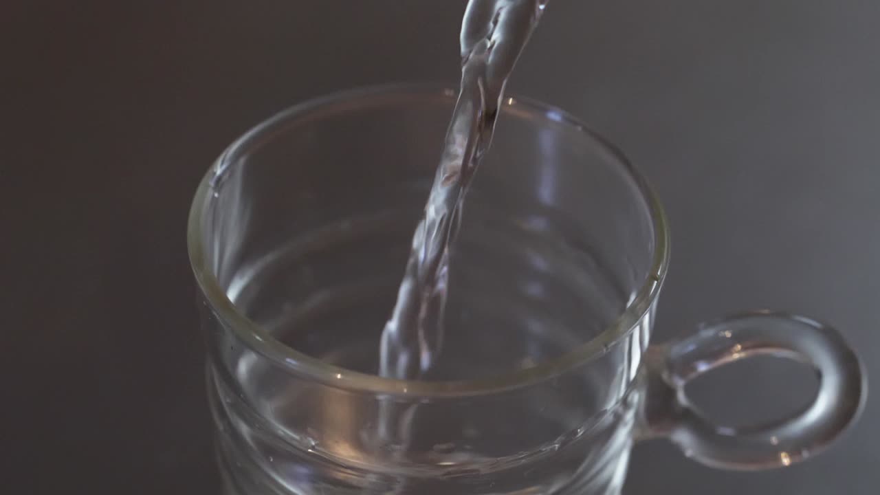 Above angled close up of water being poured into a glass cup on a metallic kitchen worktop, health and clean water concept, slow motion footage