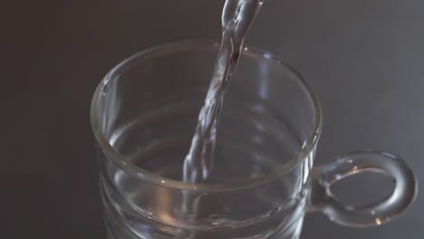 above angled close up of water being poured into a glass cup on a metallic kitchen worktop, health and clean water concept, slow motion footage