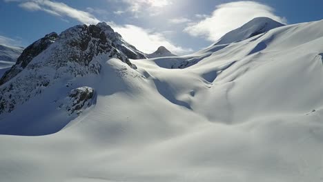 drone flying across high alpine snowfield towards huge mountains