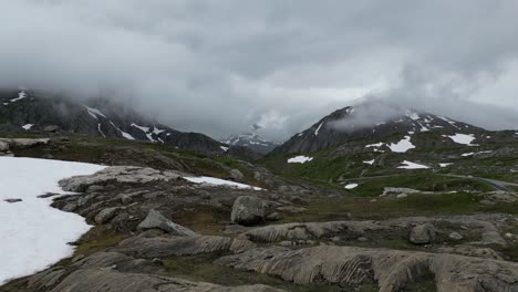 Paisaje-Aéreo-Escandinavo-De-Montaña-Con-Hierba-Verde,-Rocas,-Nieve,-Carretera,-Noruega