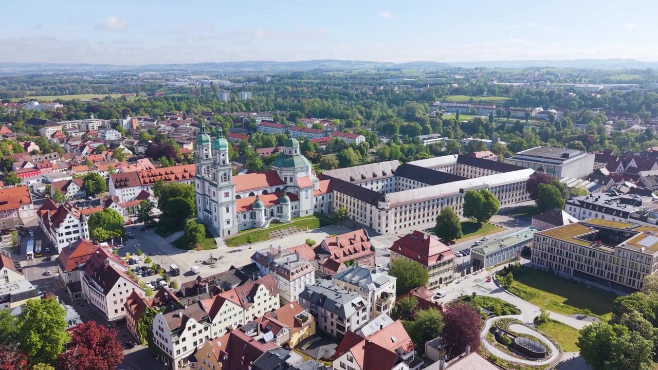Ripresa rivelatrice con drone di Kempten in Baviera, con la Basilica di San Lorenzo circondata da edifici storici e un paesaggio urbano verde sotto la luce brillante del giorno, UHD
