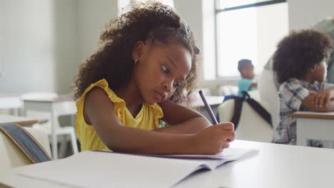 Video-of-focused-african-american-girl-sitting-at-desk-during-lesson-in-classroom