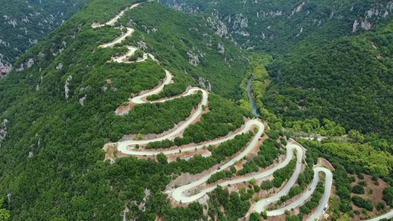 Cinematic drone shot of the famous winding road with hairpin turns in Papigo. High-angle view of the zig-zag route through lush green forest in Epirus. Perfect for travel and automotive films