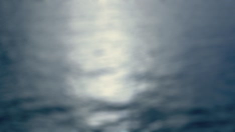 luz de la luna - bucle sin costuras de una toma de 4k completamente desfocada de una superficie de agua ligeramente ondulada. la luz de la luna pálida reflejada está brillando en la superficie del agua