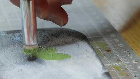 close-up of an artist's hand mixing green paint on a palette