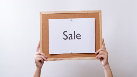 woman's hand shows the paper on board with the word sale in white studio background with copy space