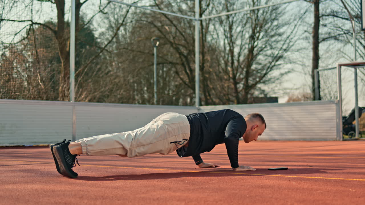 Un uomo sta facendo sport su un campo sportivo all'aperto. In estate, si dedica al proprio corpo svolgendo esercizi per la tonificazione e il miglioramento della forma fisica.