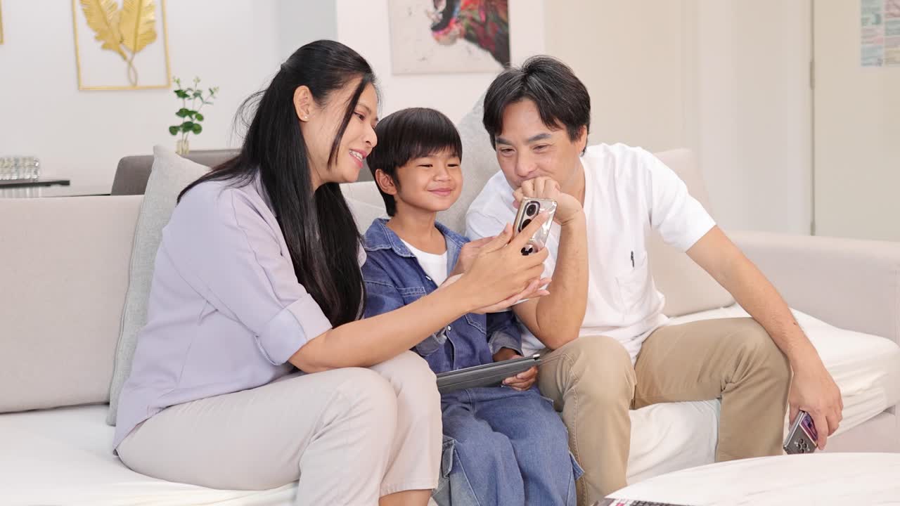 Asian family of three smiling and bonding over smartphone in bright, cozy modern living room