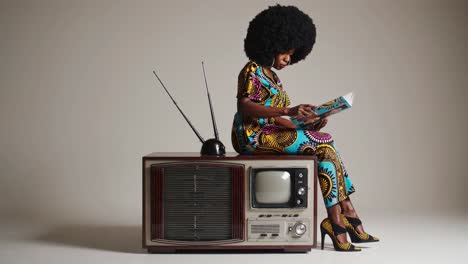 woman in 1970s fashion reading a magazine on a vintage tv