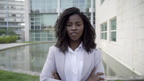 confident businesswoman with crossed arms standing near office