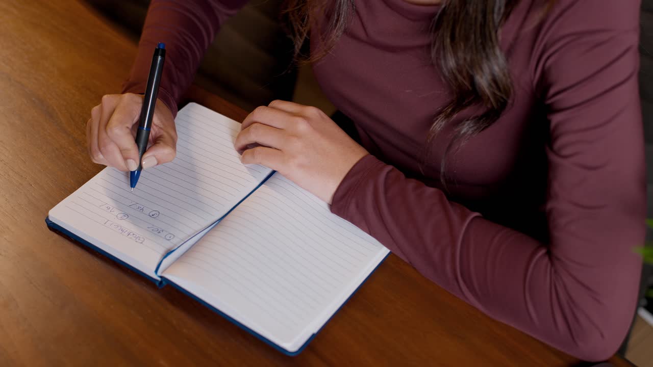 Top view woman writting, closing and reopening notebook on wooden desk