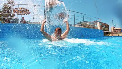 happy man enjoys time in the swimming pool. joyful man standing under the artificial waterfall in the pool in a sunny summer day.