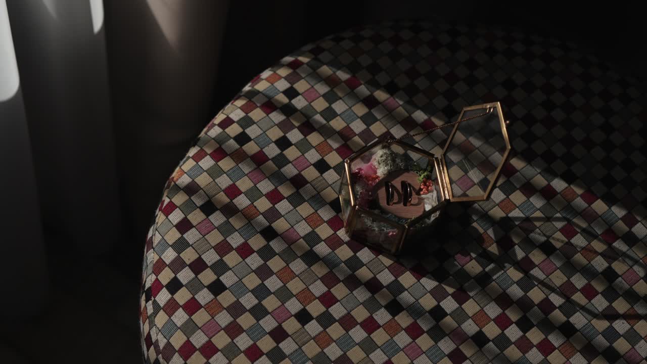 Wedding rings in glass box on checkered table with natural window light