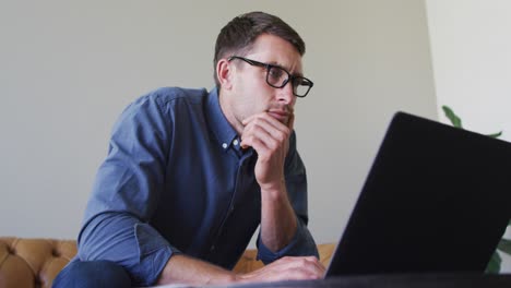 hombre caucásico con gafas trabajando desde casa usando computadora portátil