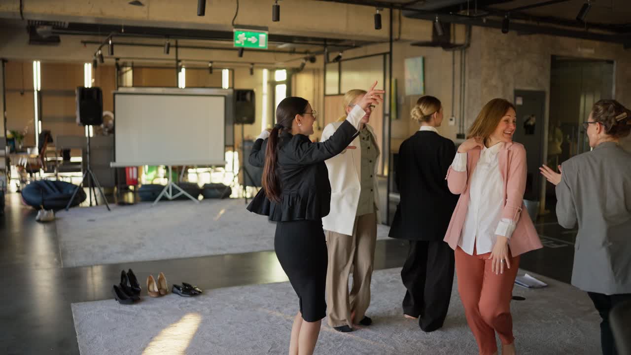 un grupo de chicas confiadas en trajes de negocios bailan durante un descanso en el trabajo en una alfombra gris durante un tiempo feliz en el traballo en una oficina moderna