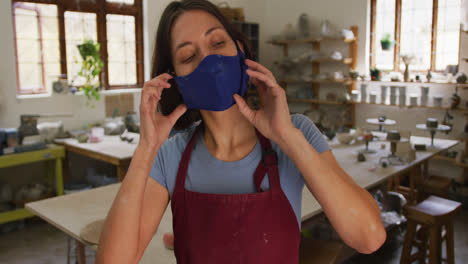 portrait of female caucasian potter wearing face mask at pottery studio