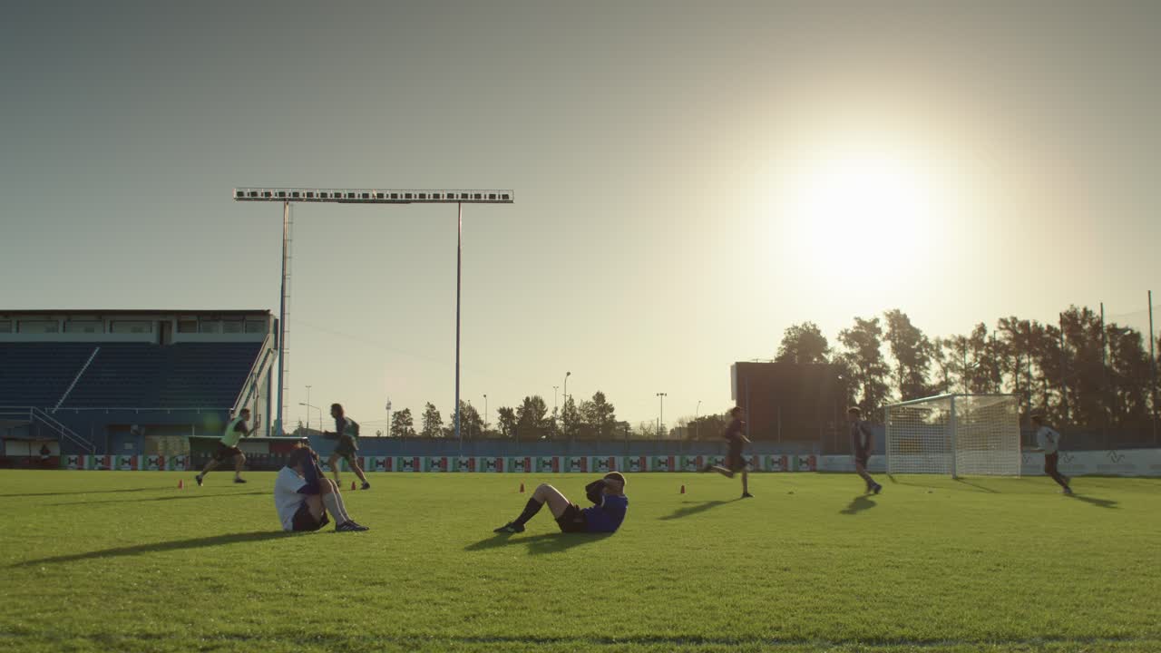 Athletes warm up on a sunny football soccer field as the day begins, preparing for practice