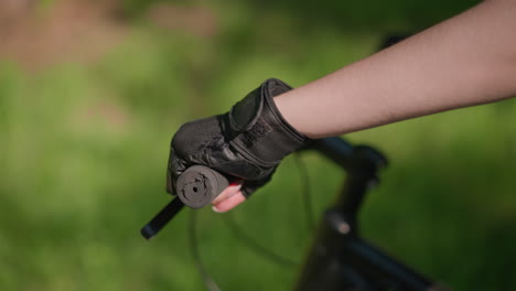 closeup of individual gripping bike handlebar with gloved hand, throttle and brake in use, sunlight gently reflects off gloved, creating focused scene set against a softly blurred green background