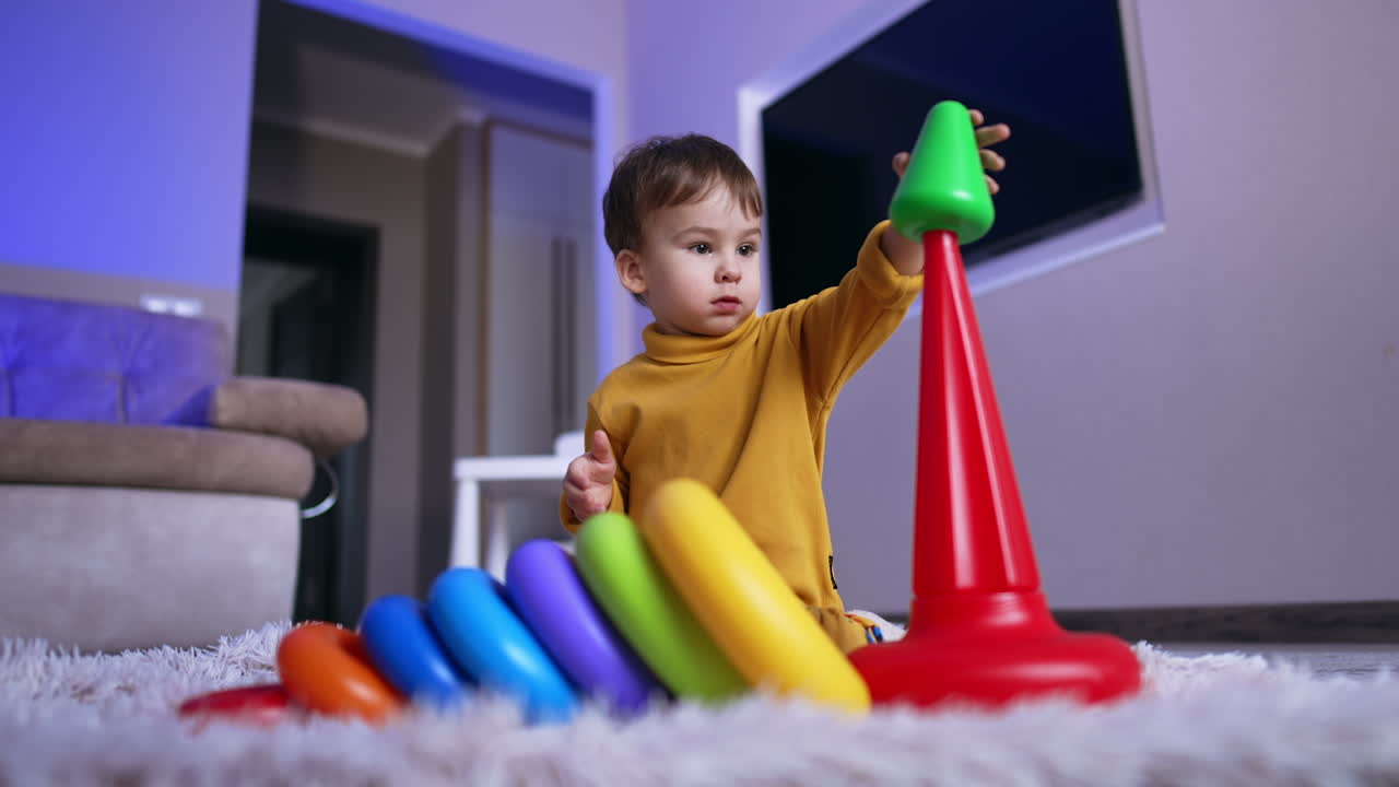 Adorable focused toddler boy collecting toy pyramid. Calm kid playing in his room at home. Low angle view.