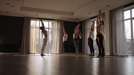 En-Cámara-Lenta,-Un-Grupo-De-Mujeres-Juntas-Hacen-Yoga-De-Diferentes-Edades-Y-Categorías-De-Peso,-Mujeres-Delgadas-Y-Gordas-En-El-Gimnasio-Por-La-Mañana-Bajo-El-Sol.-El-Resplandor-Del-Sol-En-El-Suelo