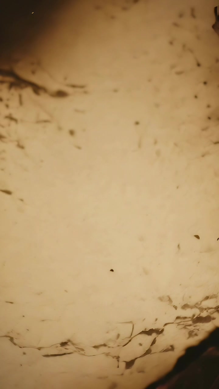 Video verticale: Telecamera che si sposta mostrando un primo piano di una superficie beige chiaro, rivelando macchioline, fibre e un bordo.