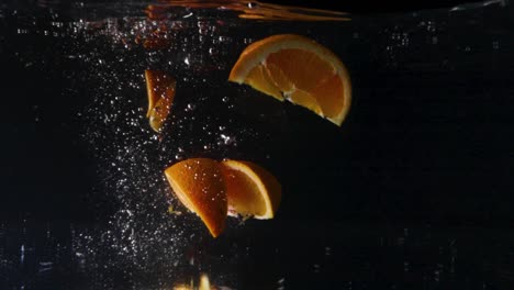 close up underwater shot of fresh orange slices falling into the water with bubbles and a black background, slow motion cut out