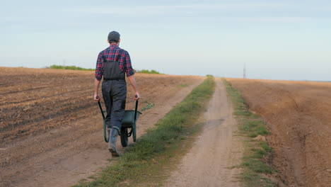 farmer pushing wheelbarrow on a dirt road