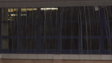 torrential rain overwhelms a guttering system and pours down in torrents in front of a building window during a thunder storm