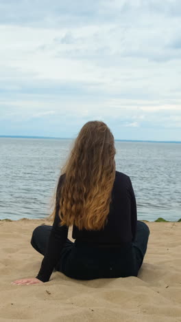 woman sitting on a beach, looking at the ocean