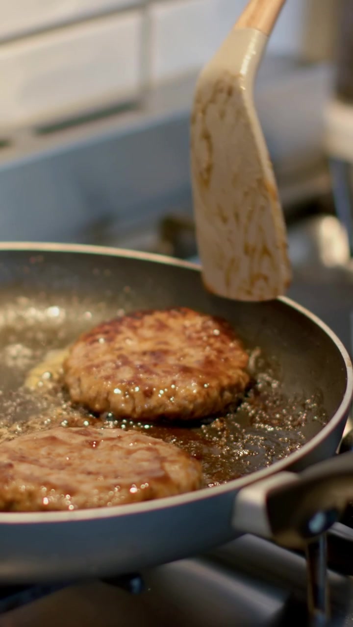 Vertical video: Sliding wooden spatula, cook's hand nudging patties on gas stove testing doneness