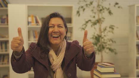 feliz anciana dando pulgares hacia arriba dentro de la biblioteca, primer plano - retrato de una mujer de envejecimiento positivo en el interior