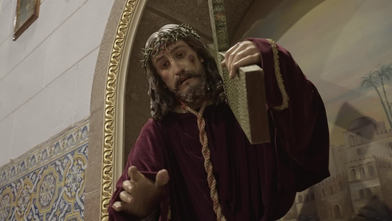 Scena interna di chiesa con statua religiosa di Gesù Cristo che indossa una corona di spine e porta la croce, simboleggiando la crocifissione e la fede cristiana.