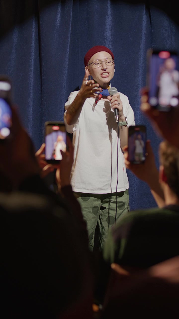 Female Stand Up Comedian Performing on Stage and Viewers Recording with Phones