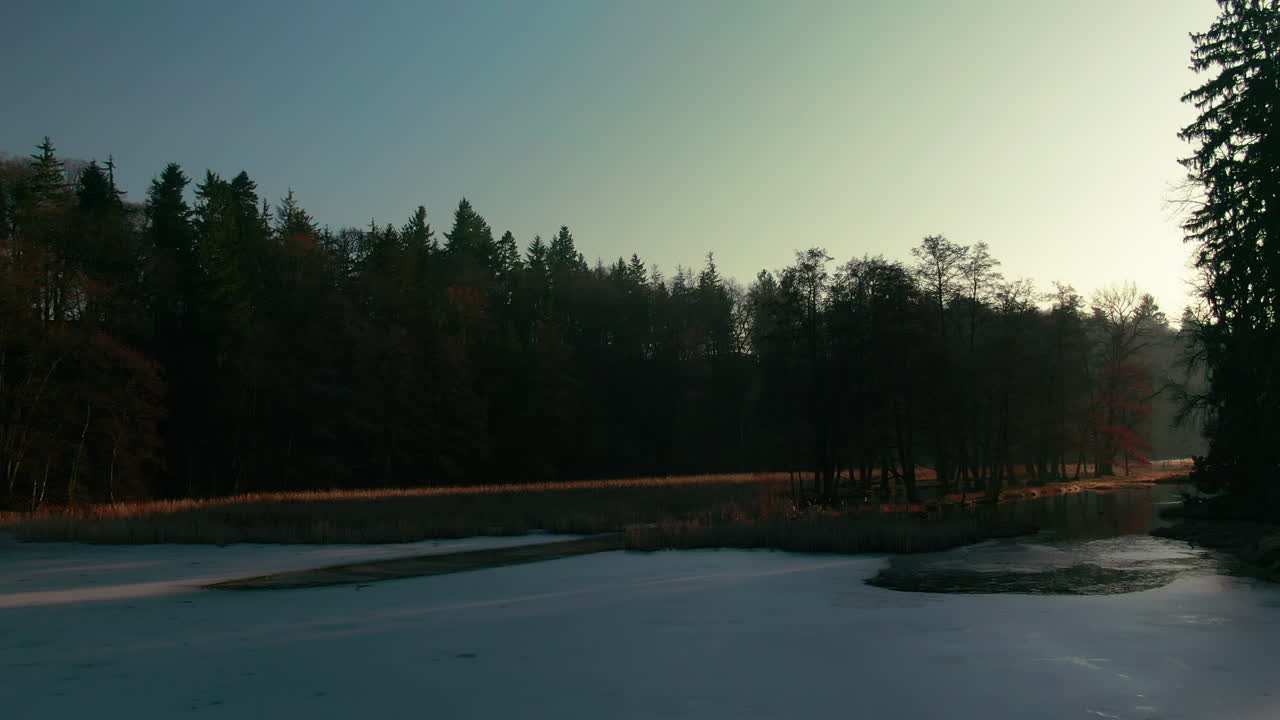 winter lake drone flight aerial frozen water forest pine trees sunset sunlight light rays pruhonice czech republic