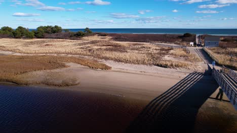 Beach-and-bridge-flyover-of-a-coastal-river-towards-the-open-Atlantic-Ocean-with-sun-and-blue-skies