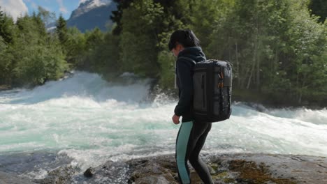 Reisende-Frau-Mit-Rucksack,-Trinkwasser-In-Der-Natur-Im-Wald-In-Der-Nähe-Eines-Gebirgsflusses.