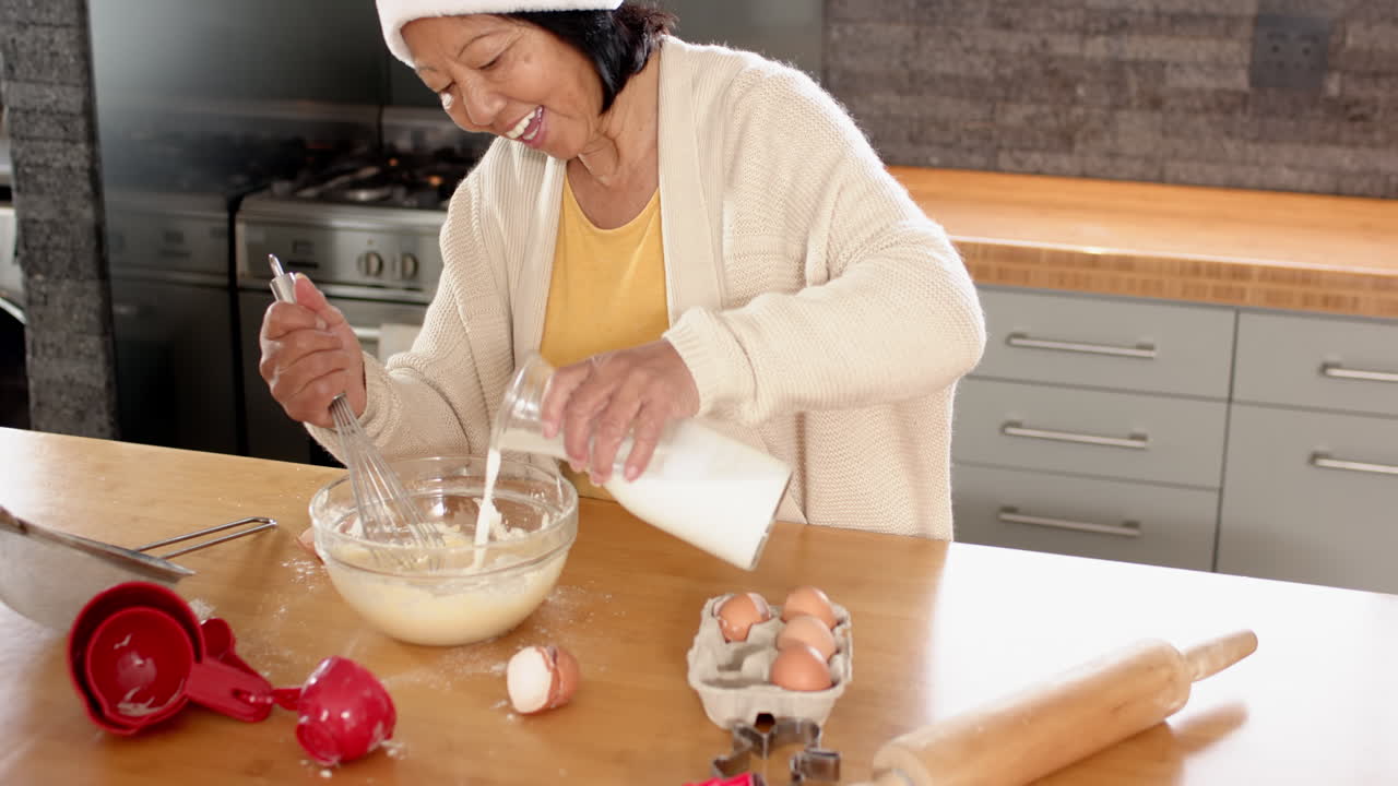 Senior Asian woman happily baking at home, mixing ingredients in kitchen