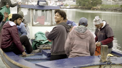 hand held medium shot of fishing industry workers embarking on a small boat in hout bay, south africa on their way to work. sunny daylight shot of blue collar workers.