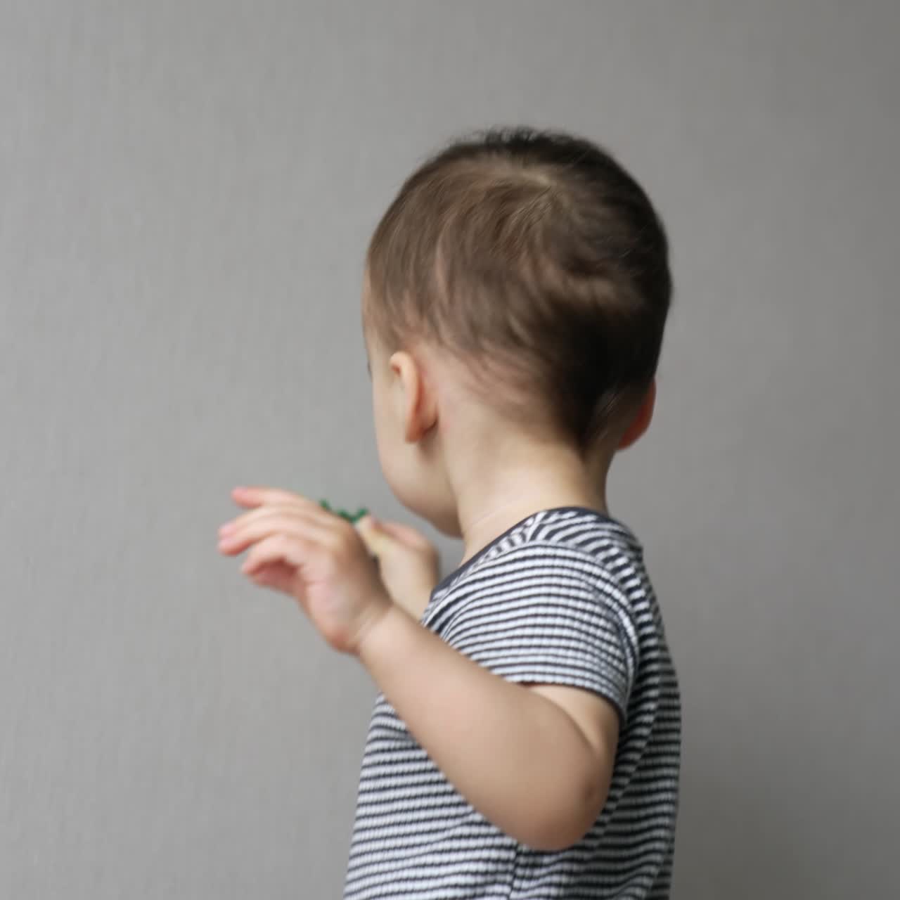 Sweet kid walks by the room holding a toy. Toddler boy moves by the house looking around. Low angle view