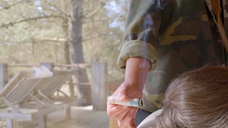 Terapeuta-De-Medicina-China-Que-Trae-La-Cabeza-Del-Paciente-Con-Un-Cigarrillo-De-Hierbas,-Al-Fondo-Se-Puede-Ver-Un-Bosque-De-Pinos