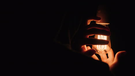 back view of man warming his hands near a light bulb in the dark