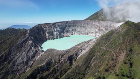 aerial closeup of the rim of a steaming volcano ijen with a turquoise lake, and foggy cloudy mountain in the background - east java, indonesia